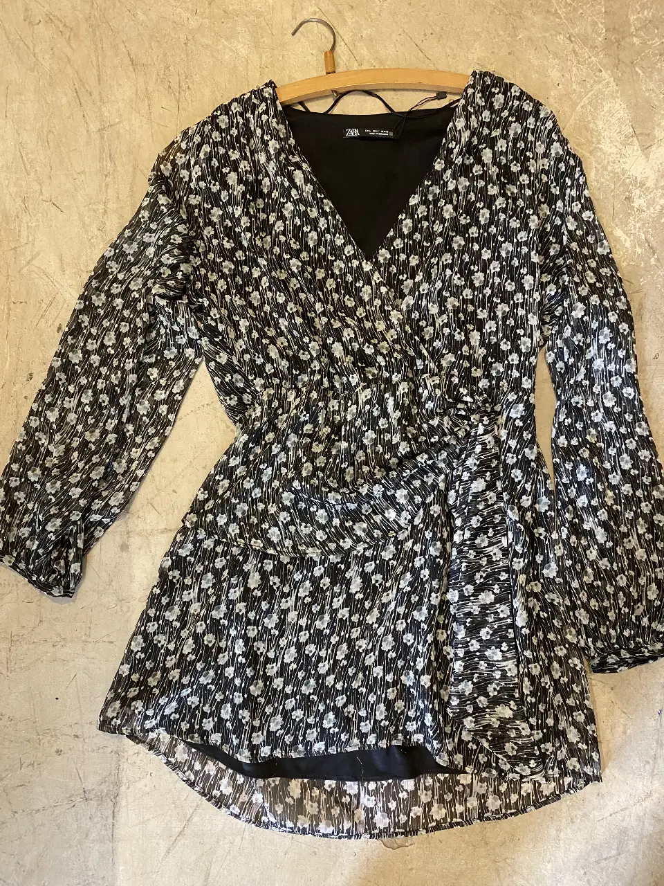 Vestido mini con estampado floral en blanco y negro, de manga larga y corte cruzado. Ideal para un look elegante y moderno.