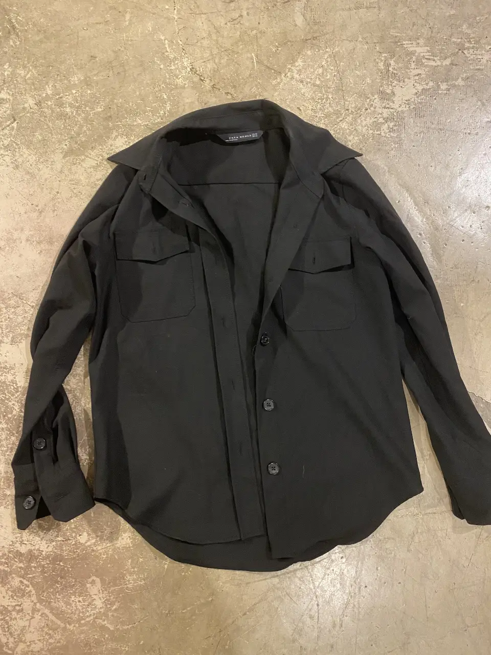 Camisa negra de mujer, manga larga, con dos bolsillos delanteros y cuello clásico. Ideal para un look casual o semi formal.