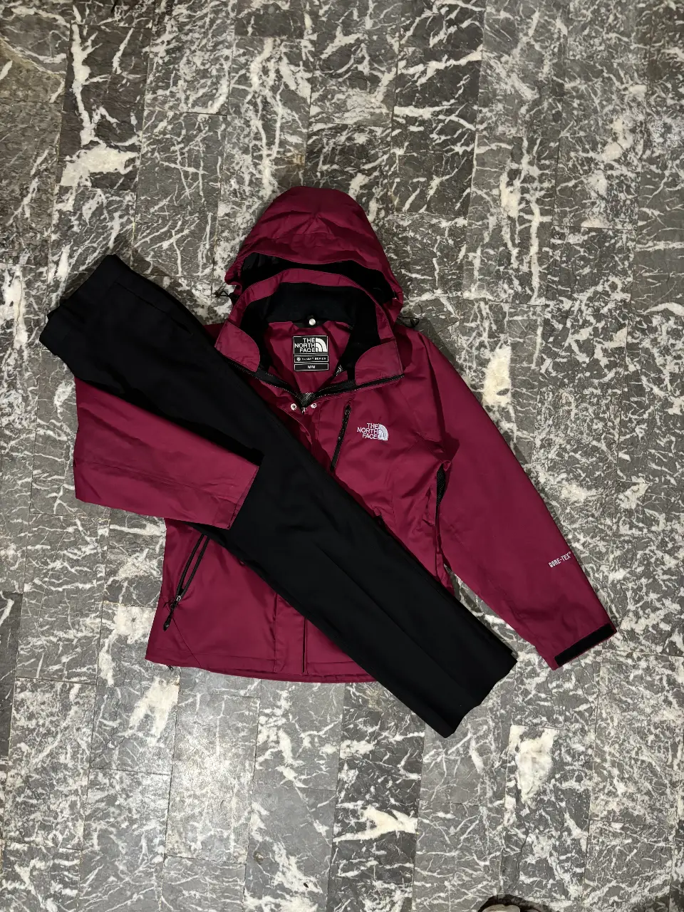 Campera deportiva The North Face color bordó con capucha y cierre, junto con un pantalón negro. Ideal para actividades al aire libre y protegerse del frío.