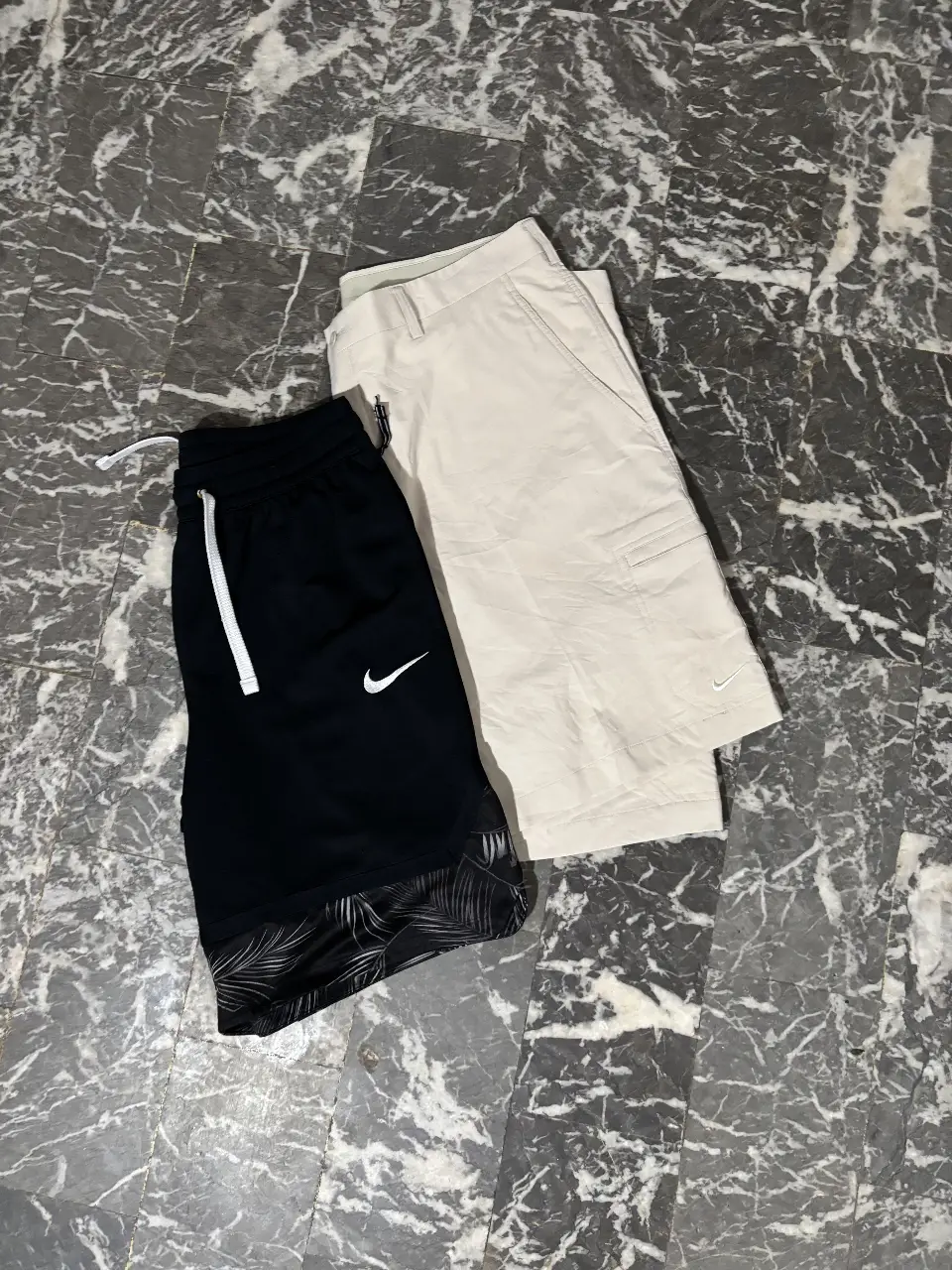Shorts deportivos Nike, uno negro L con logo blanco y detalles en la parte inferior, y otro beige XL con bolsillo lateral y logo blanco.