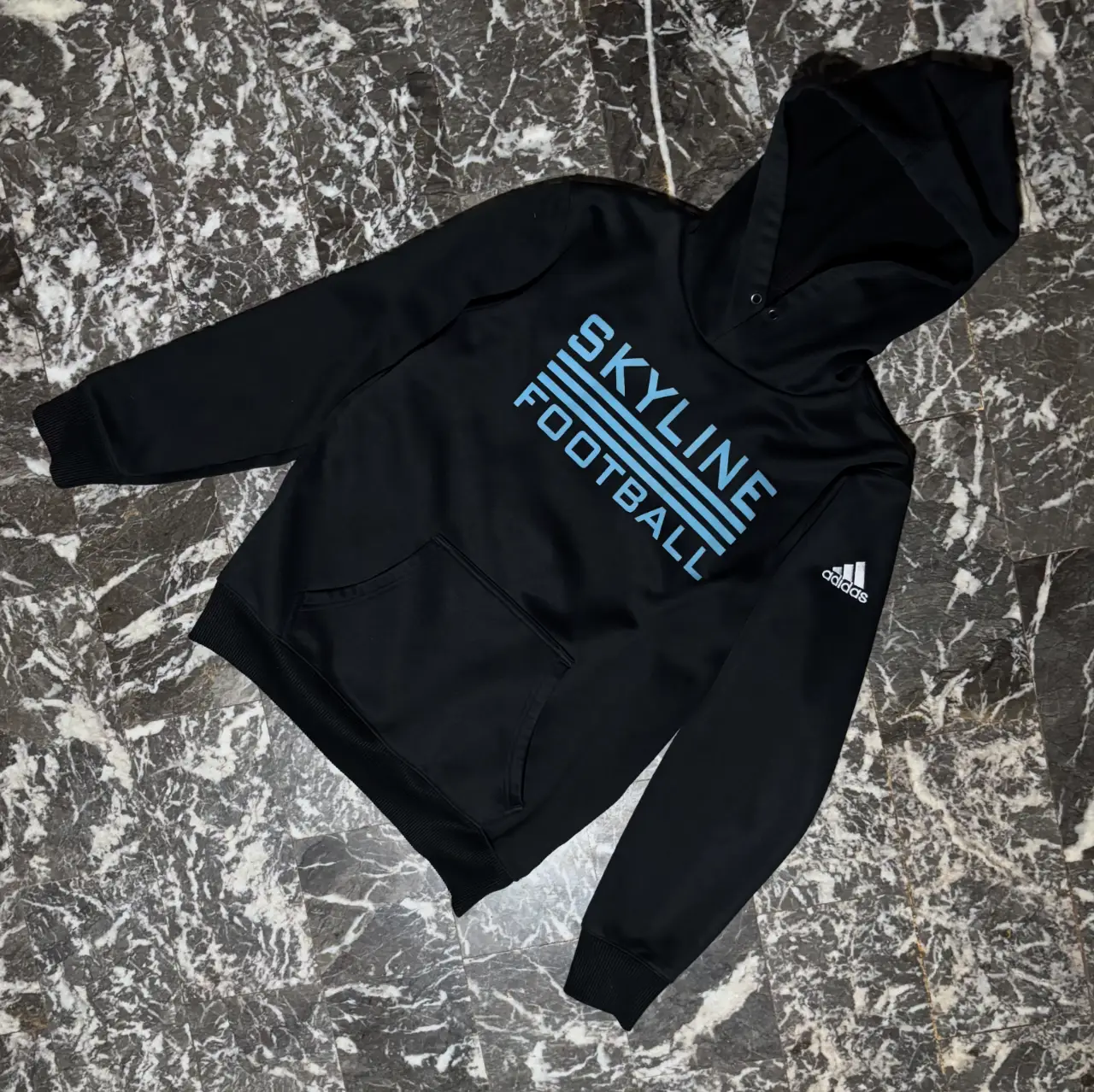 Buzo canguro negro de hombre con capucha y el logo de Skyline Football en celeste. Ideal para entrenar o usar en el día a día.