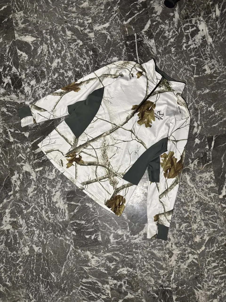 Buzo con cierre para hombre, con estampado de camuflaje invernal. Ideal para actividades al aire libre y caza. Con detalles en gris oscuro y logo de la marca Realtree