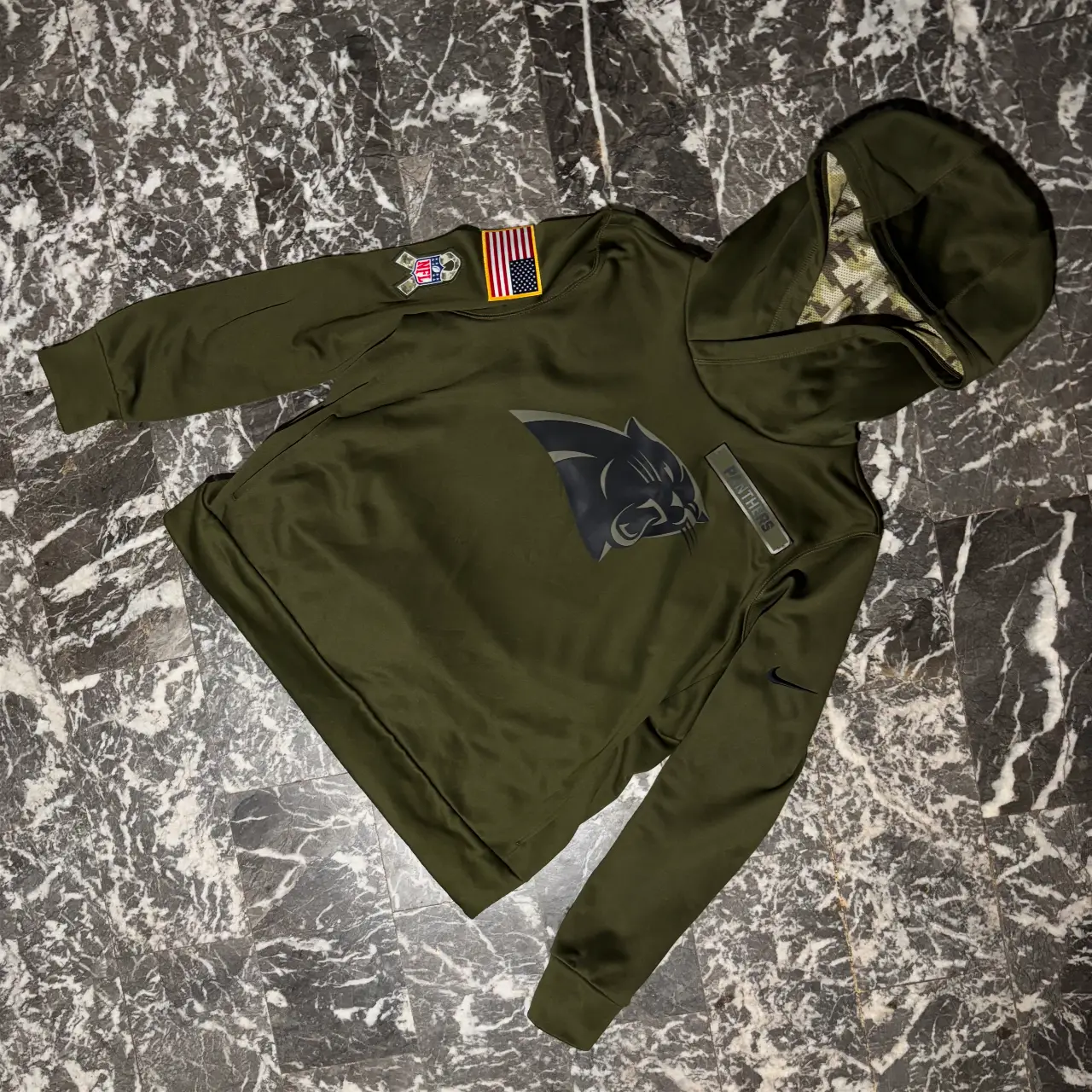 Buzo con capucha de color verde oscuro, con el logo de los Panthers en el pecho. Posee parches en las mangas y un diseño camuflado en el interior de la capucha. Ideal para un look deportivo y casual.
