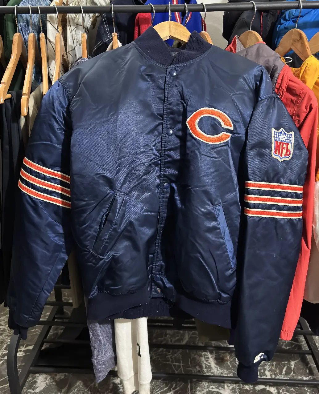 Campera bomber de los Chicago Bears, de color azul marino con detalles en naranja y blanco. Con el logo del equipo en el pecho y el logo de la NFL en la manga. Ideal para los fanáticos del fútbol americano y para un look casual y deportivo.
