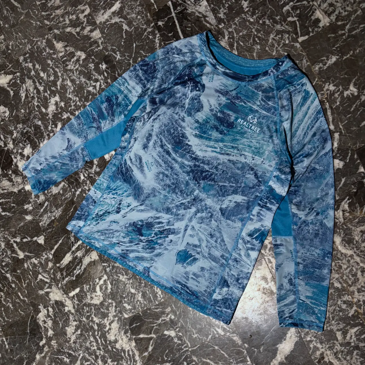 Remera manga larga deportiva para hombre, con estampado de diseño acuático en tonos azules y blancos. Ideal para actividades al aire libre. Realtree