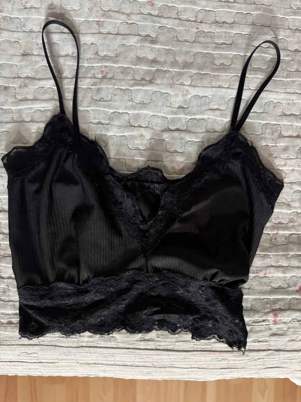 Top negro con tiras finas y detalles de encaje en el borde superior y en la cintura.