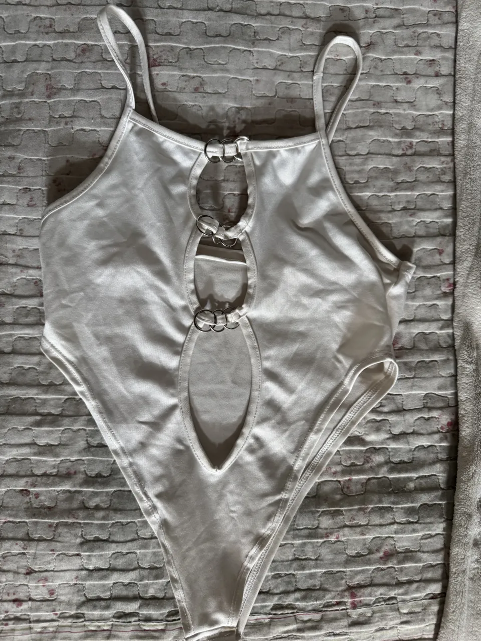 Body blanco con tiras finas y detalle de argollas metálicas en la parte delantera.