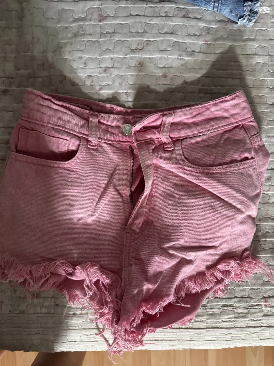 Shorts de jean color rosa con roturas y flecos en el ruedo. Cierre y botón.