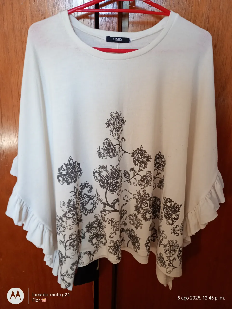 Blusa de mujer de color blanco con estampado floral en tonos oscuros. Diseño con mangas amplias y volados en los bordes, ideal para un look casual y fresco.