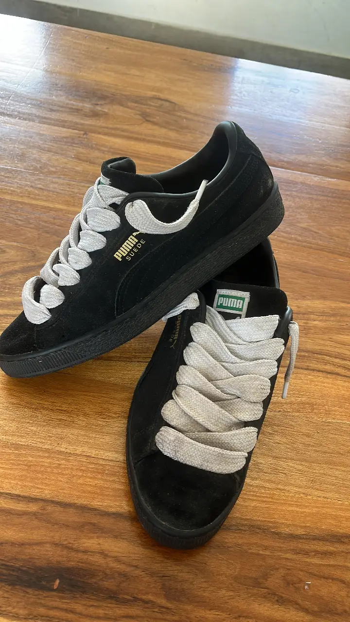 Zapatillas Puma Suede negras con cordones grises. Un clásico de Puma, ideales para un look casual y urbano. Su diseño atemporal las convierte en un calzado versátil para cualquier ocasión.