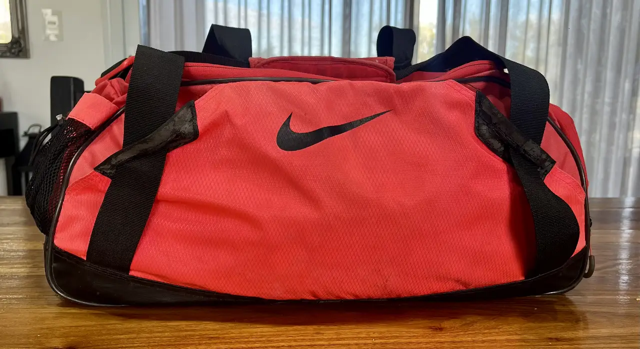 Bolso deportivo Nike en color coral con detalles en negro. Ideal para llevar al gimnasio o para viajes cortos. Cuenta con botinero incorporado, bolsillos en la parte frontal trasera  y un bolsillo de red lateral. Perfecto para el día a día.