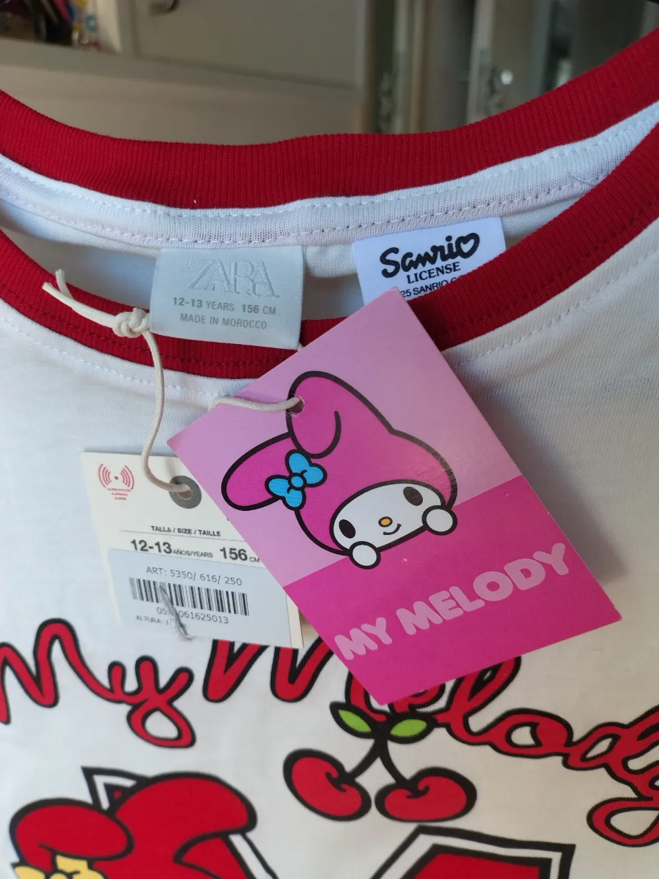 Remera blanca con cuello y mangas rojas. Estampa frontal de My Melody con la letra "M" y "Dance University".