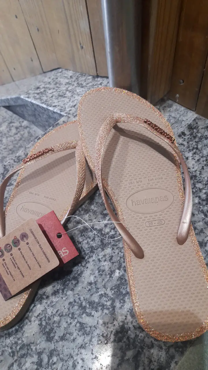 Ojotas Havaianas doradas con glitter, ideales para la playa o un look casual de verano. Tienen detalles brillantes en las tiras y el borde de la suela.