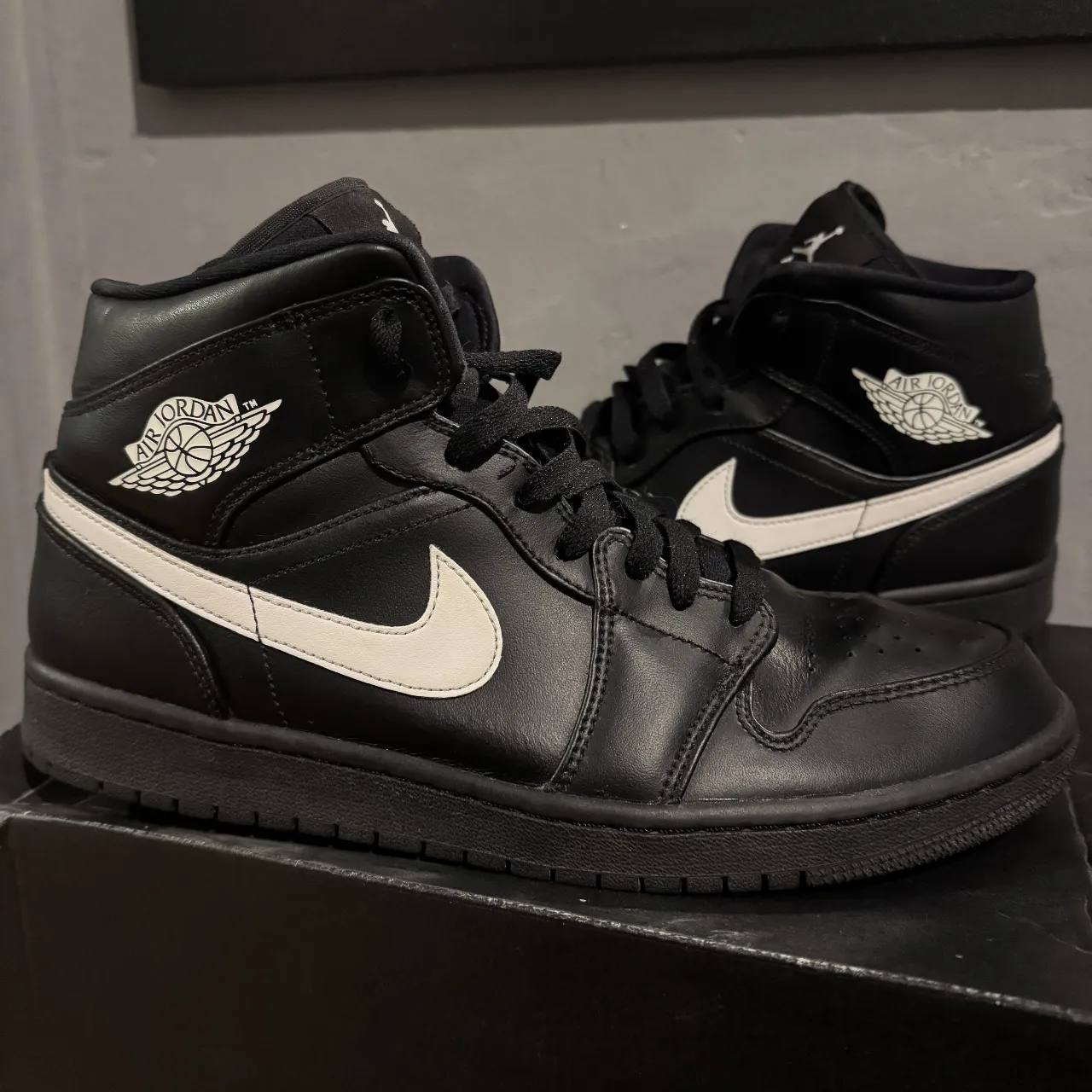 Zapatillas Air Jordan 1 Mid negras con detalles blancos. Diseño icónico y versátil para un look urbano y moderno. Ideales para combinar con cualquier outfit.