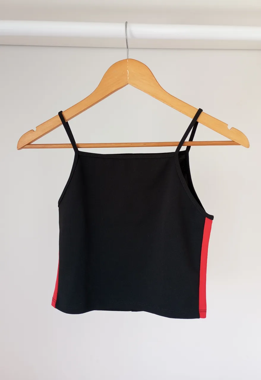 Top negro con detalles laterales en rojo. Diseño moderno y canchero, ideal para un look urbano o deportivo.