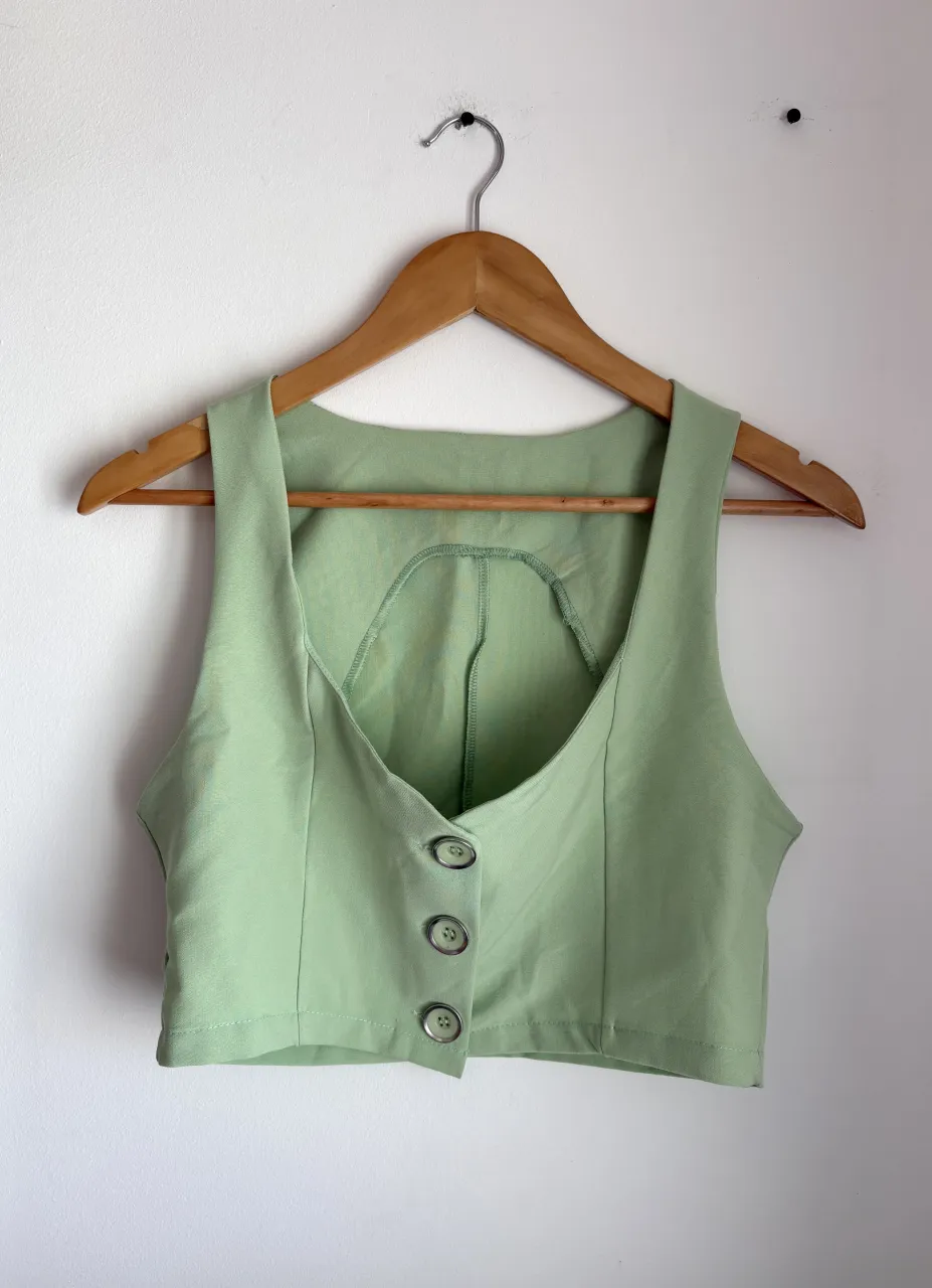 Chaleco corto de color verde pastel con tres botones al frente. Escote en V pronunciado y espalda con corte curvo.