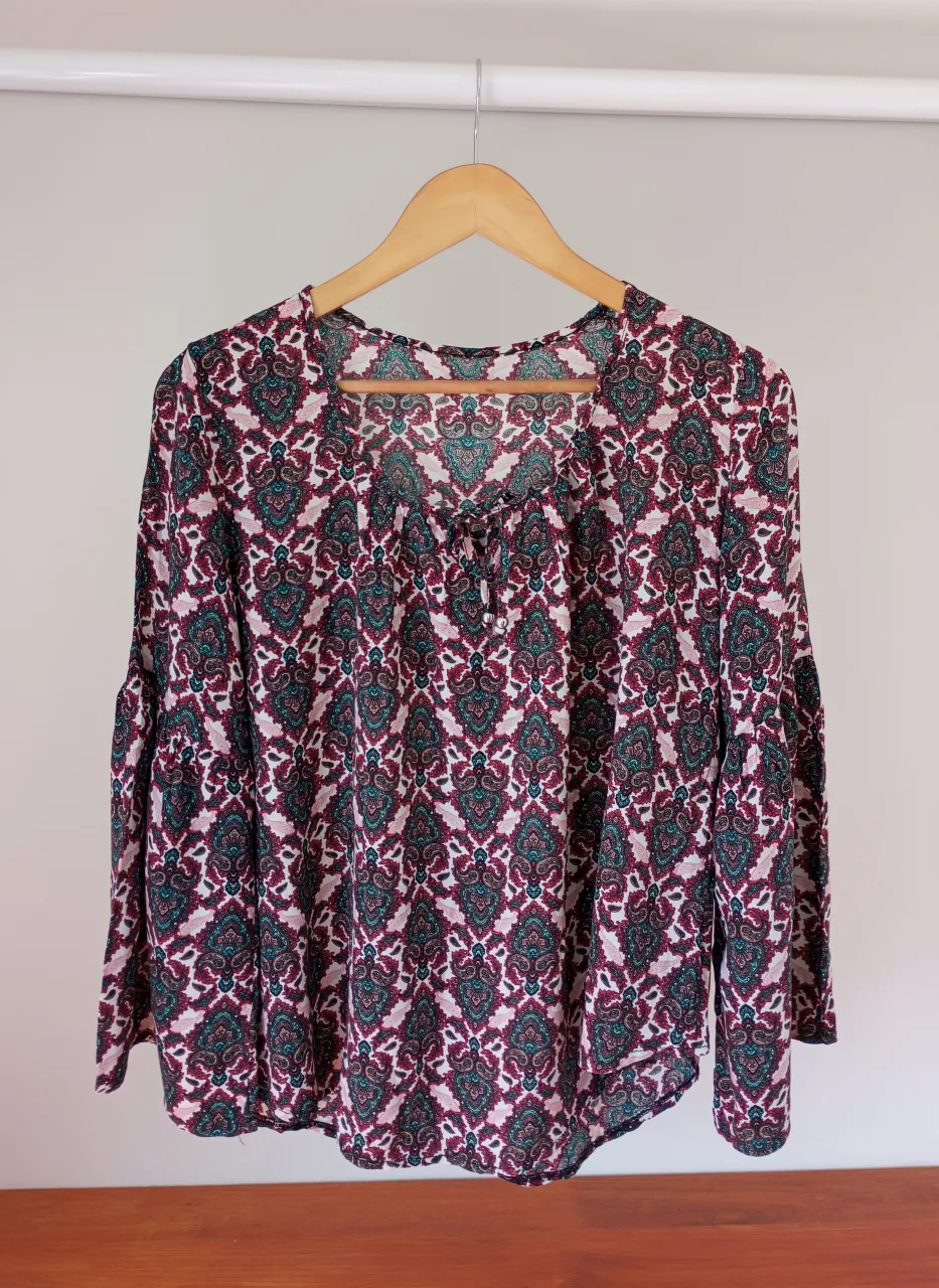 Blusa estampada con mangas largas acampanadas y detalle de lazo en el escote. Su diseño vibrante la hace ideal para un look bohemio y relajado.