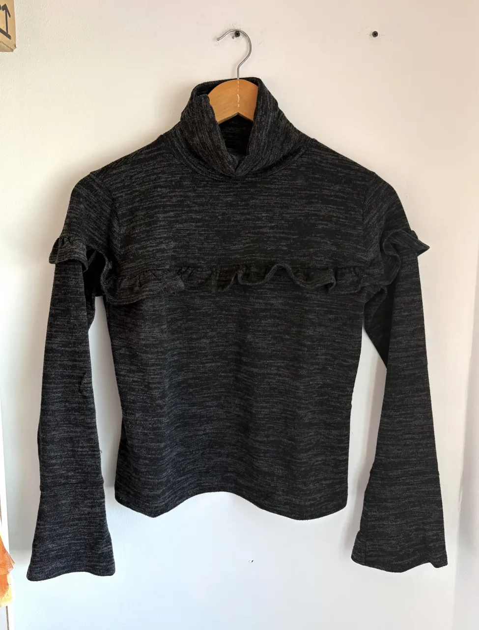 Polera de lanilla manga larga con cuello alto y volados en el frente. Posee puños acampanados.