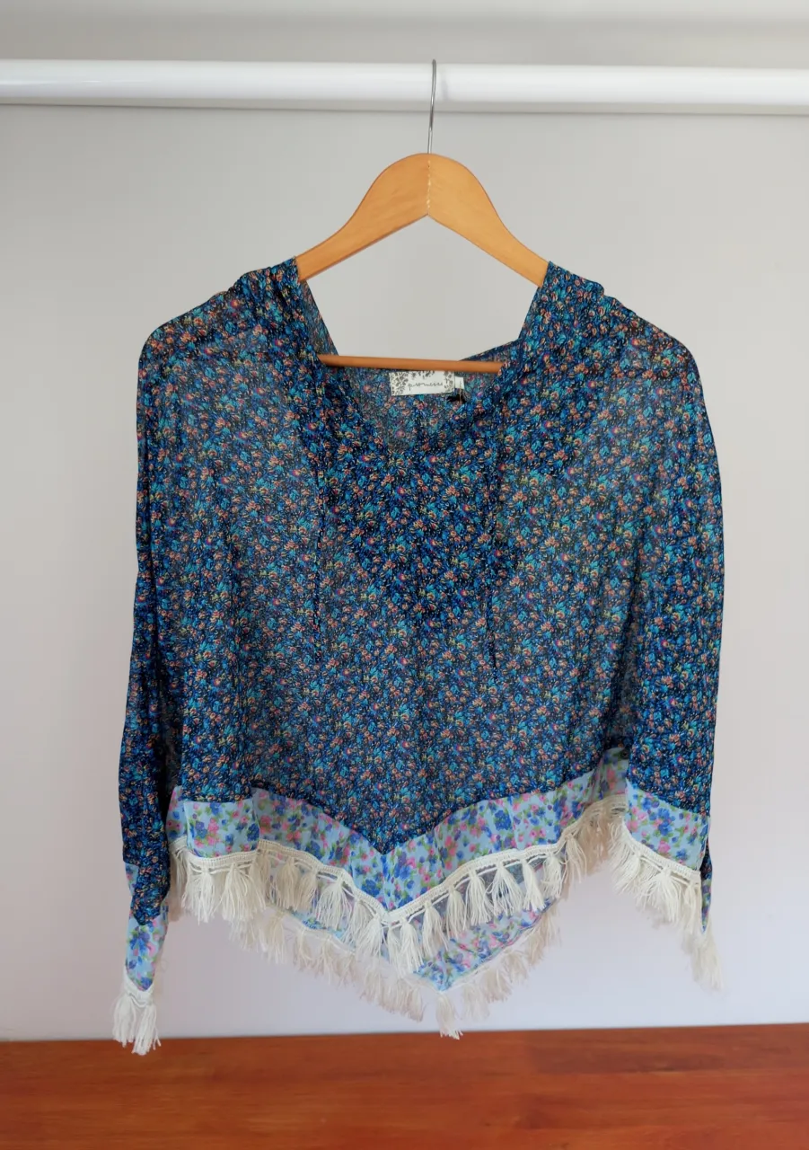 Blusa poncho de gasa con estampa floral vibrante y detalles de flecos en el borde inferior. Ideal para un look bohemio y fresco.