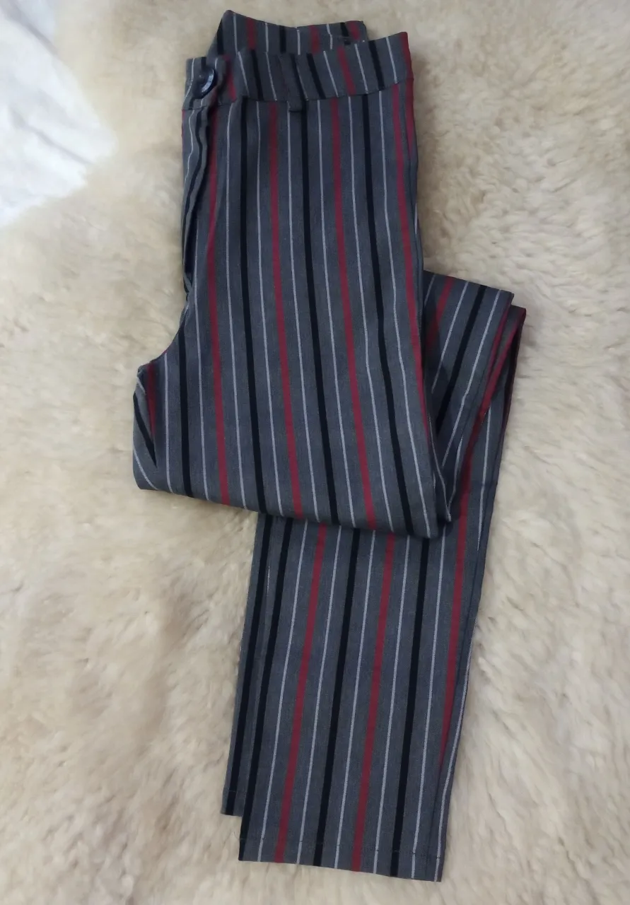 Pantalón de vestir de bengalina a rayas grises, negras, blancas y rojas. Tiro alto con botón y cierre. Corte recto y elegante, ideal para un look formal o de trabajo.