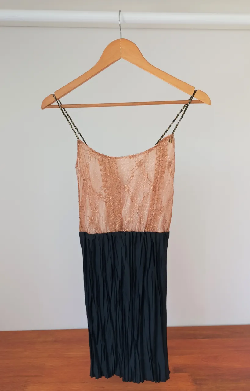 Vestido corto con tiras finas y detalles de encaje dorado en la parte superior. La falda es negra, con un plisado marcado y textura arrugada. Ideal para una noche especial o una fiesta.