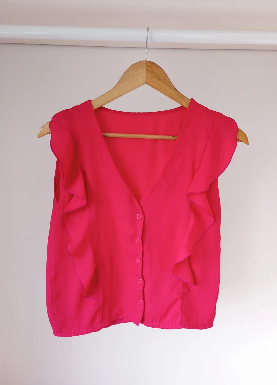 Blusa fucsia con volados en los hombros y escote en V. Posee botones al frente y es sin mangas. Ideal para un look canchero y femenino.