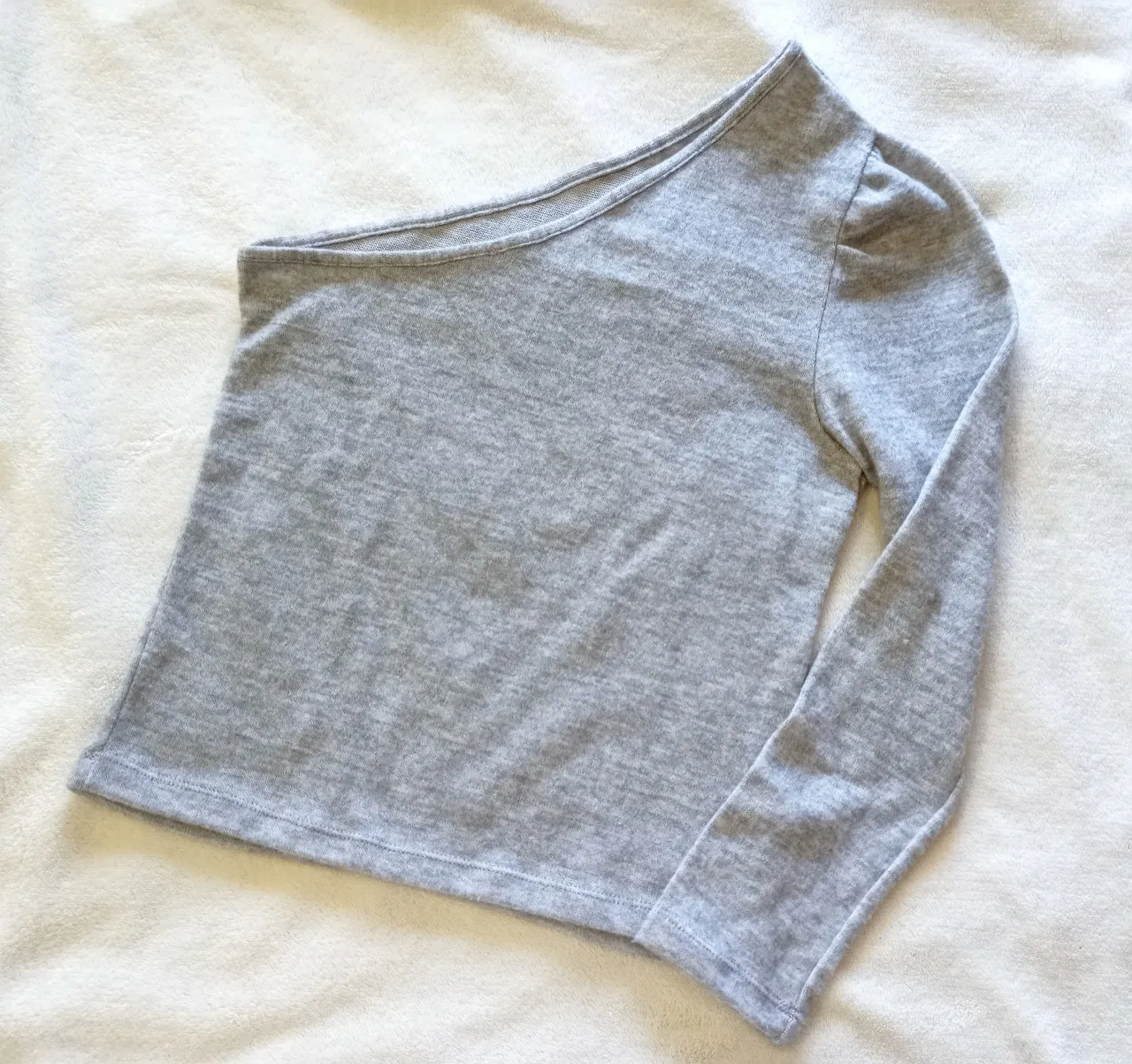 Remera gris de lanilla manga larga, con un solo hombro descubierto. Diseño moderno y canchero, ideal para looks urbanos y descontracturados.