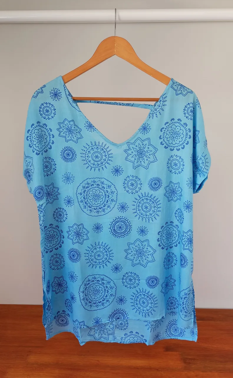 Remera súper fresca y liviana con estampa de mandalas en tonos celestes y azules. Posee un escote en V pronunciado y un detalle de tiras cruzadas en la espalda. Ideal para un look relajado y con onda.