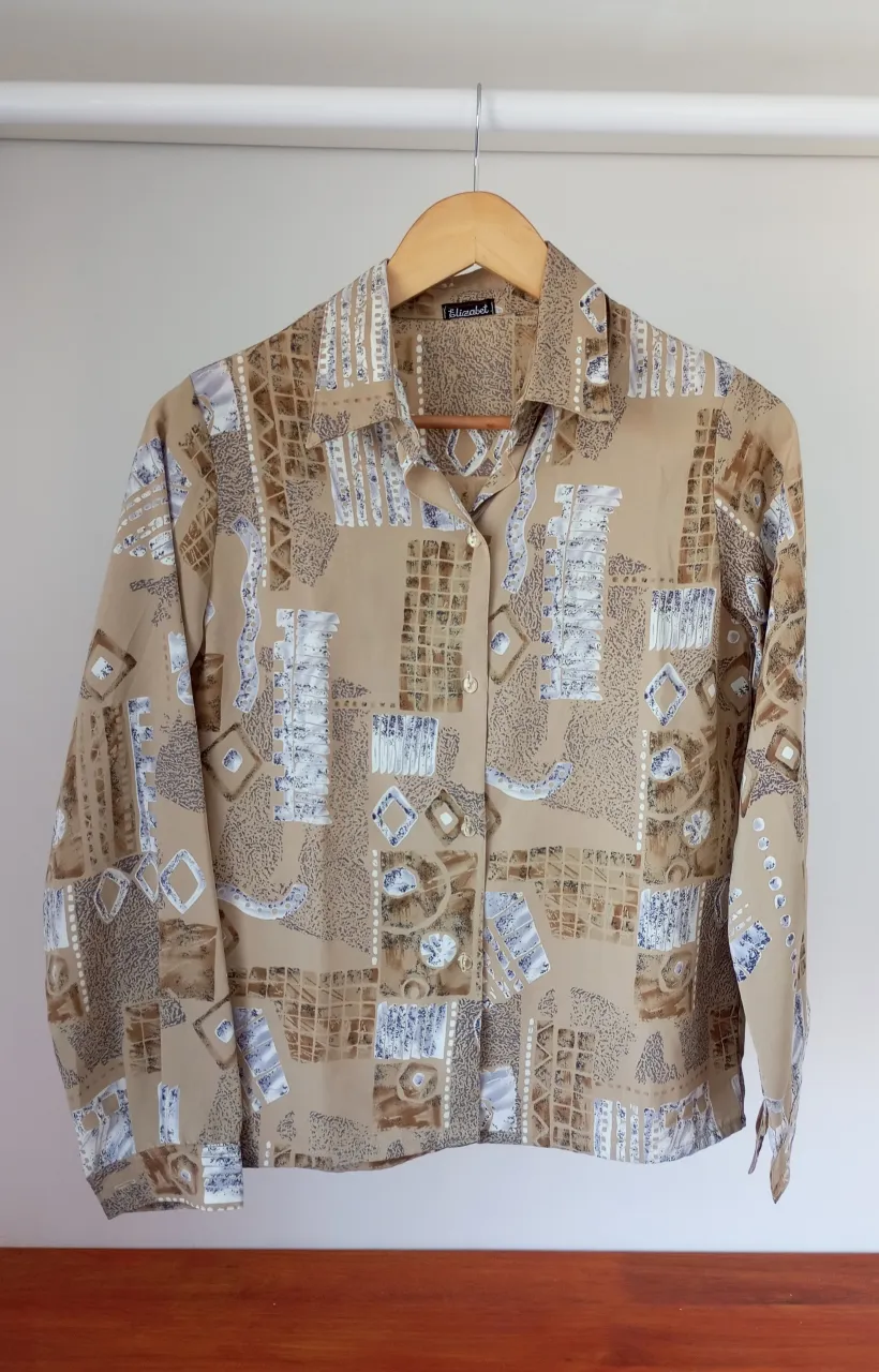 Camisa de manga larga con estampado abstracto en tonos beige, marrón y azul. Cuello camisero y botones al frente.