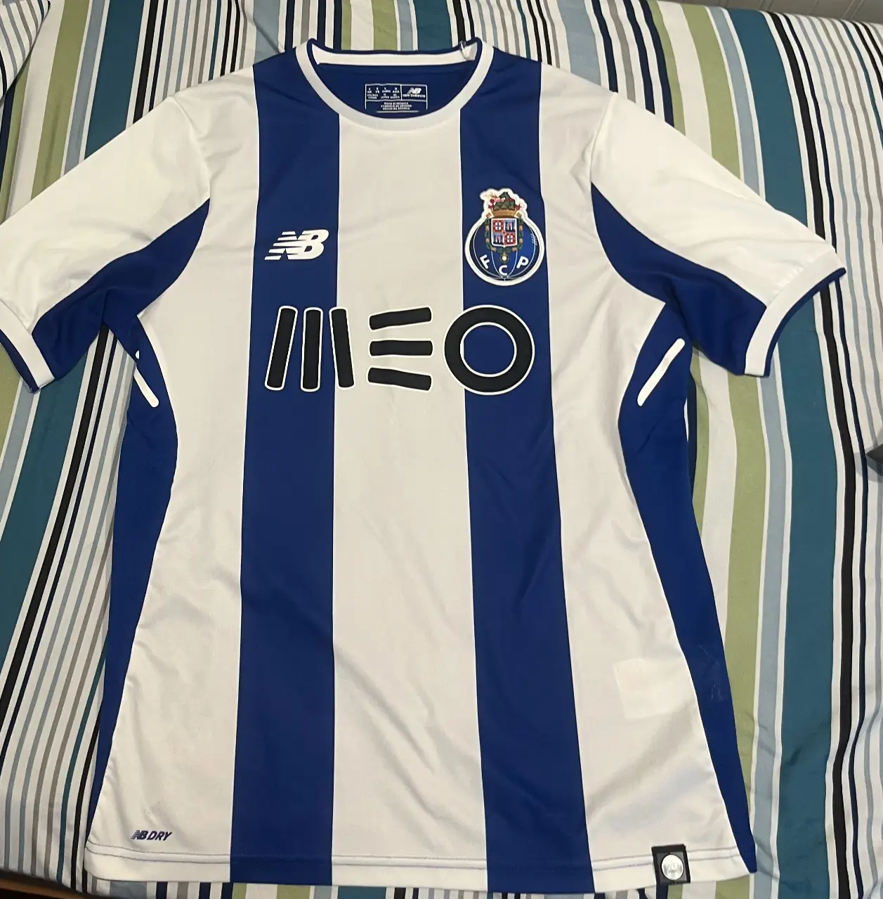 Camiseta de fútbol del FC Porto, con diseño a rayas verticales en blanco y azul. Presenta el logo de New Balance y el escudo del equipo. En la espalda, destaca la publicidad de Super Bock. Ideal para fanáticos y coleccionistas.