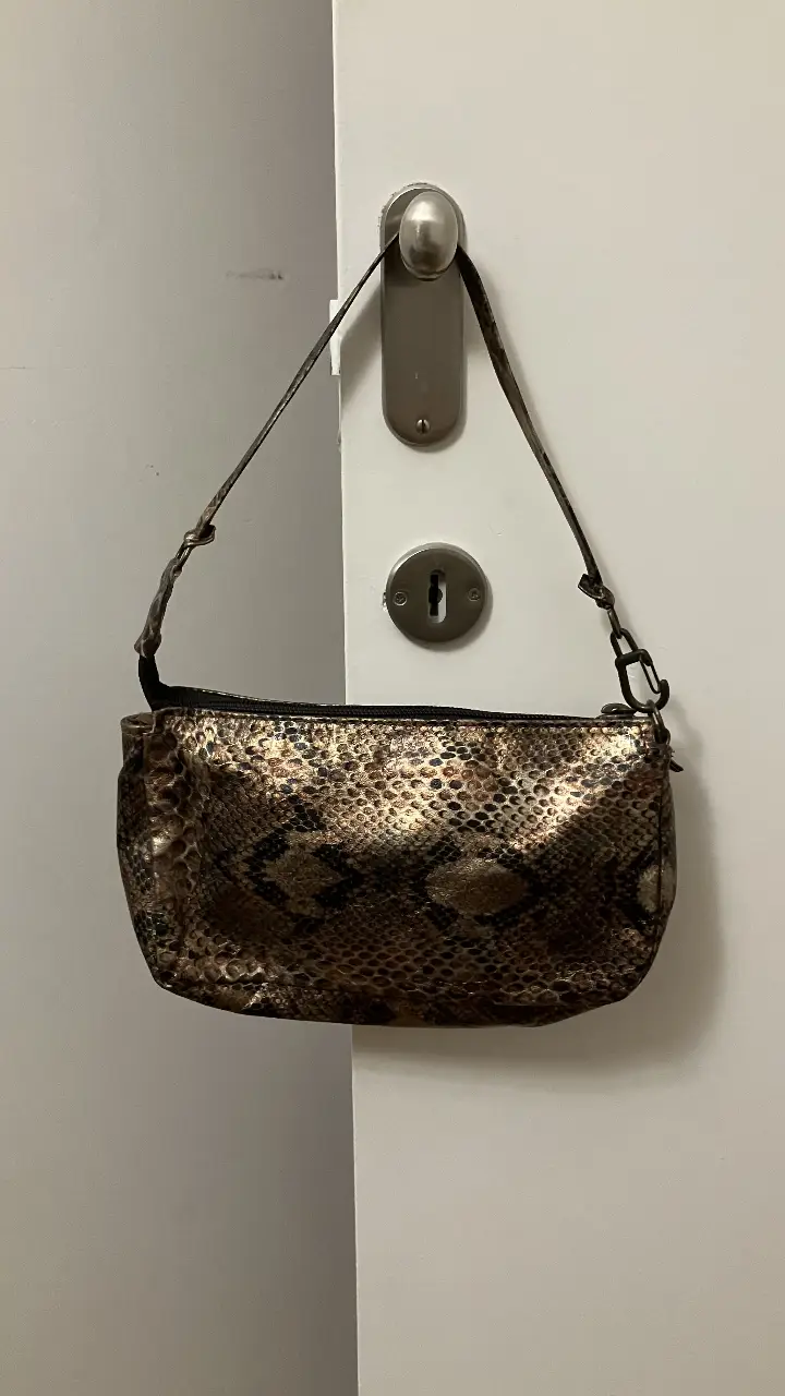 Cartera de hombro baguette con estampado de serpiente en tonos dorados y marrones. Con forro de tela y cierre en excelente estado.