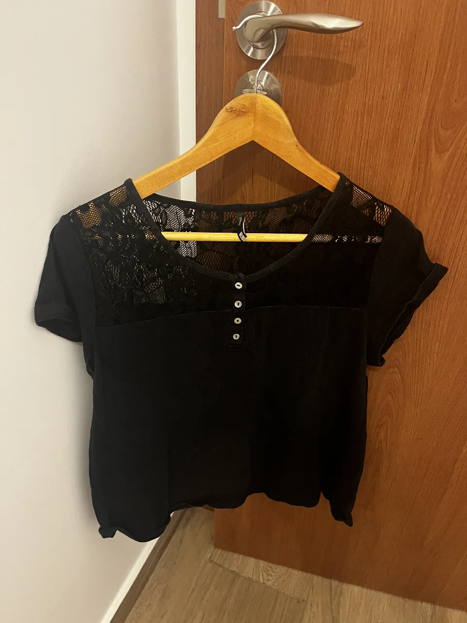 Remera negra con detalles de encaje en la parte superior y botones nacarados en el escote. Manga corta y corte moderno.