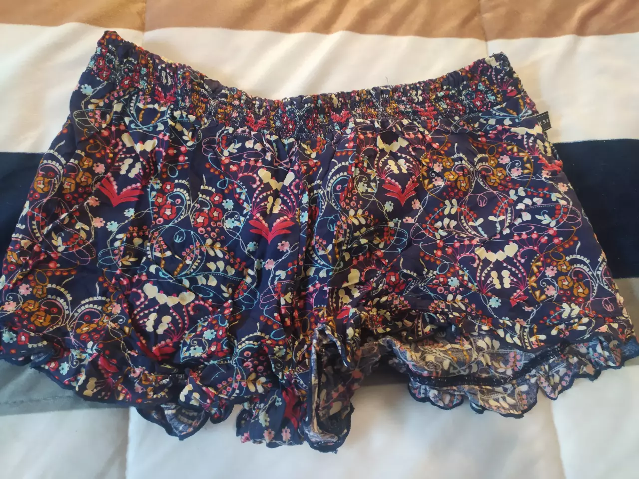 Short de tela con estampado floral en tonos azules, rojos y amarillos Kosiuko. Cintura elastizada y detalle de volados en el borde inferior. Ideal para un look fresco y bohemio.