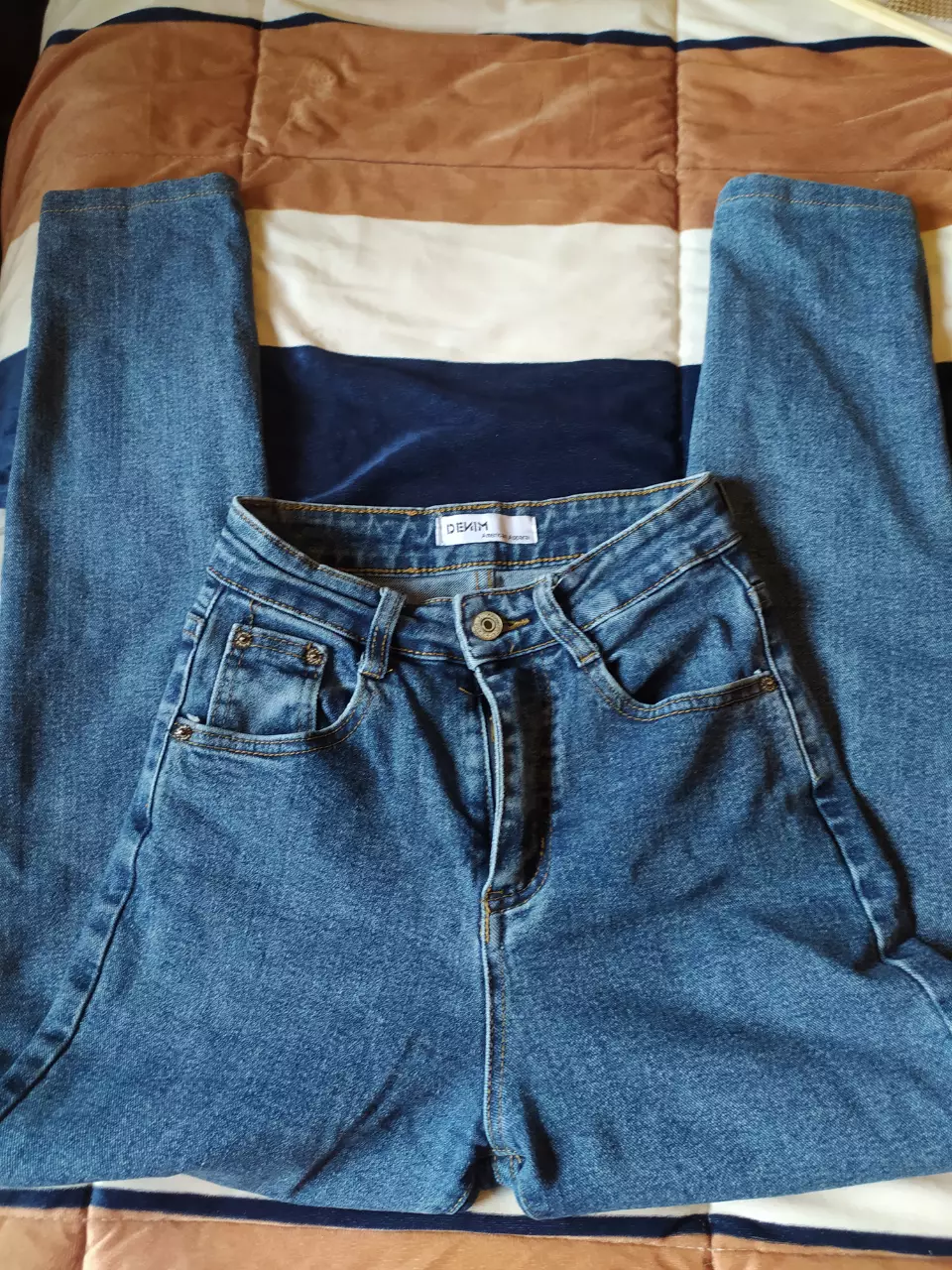 Jeans rectos de denim azul, tiro medio, con bolsillos clásicos y etiqueta de la marca American Apparel. Un básico versátil para cualquier guardarropa.