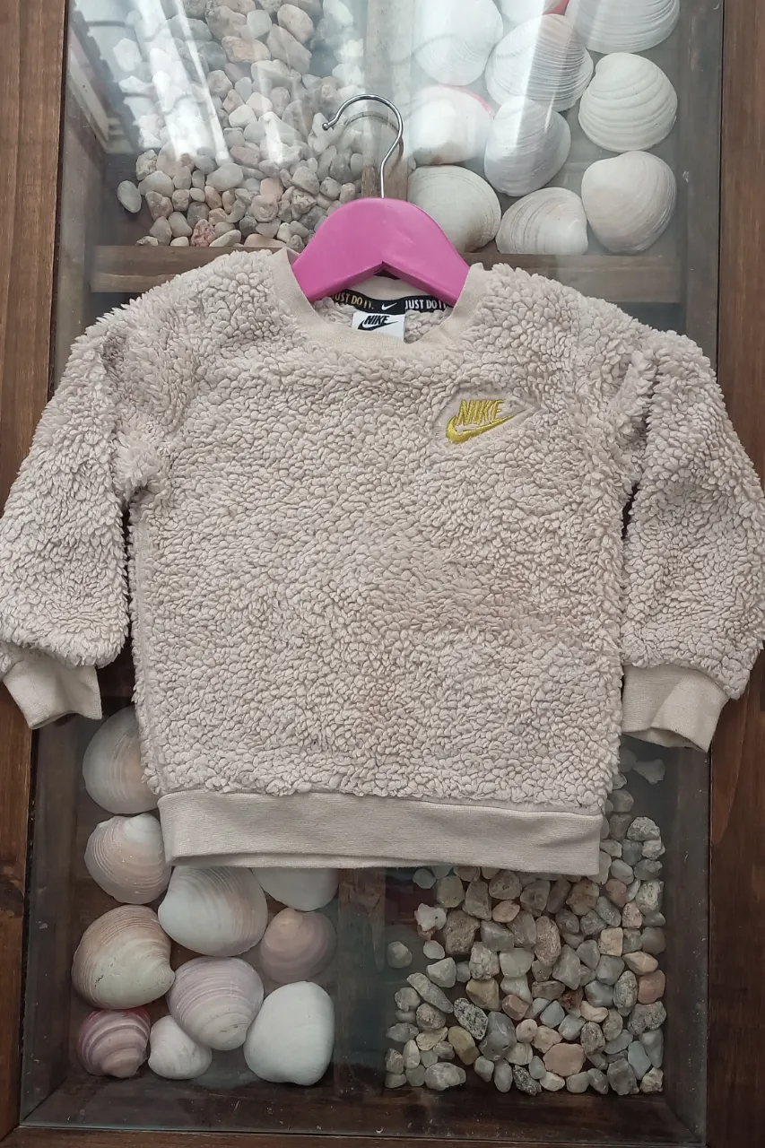 Buzo de corderito color beige con logo de Nike bordado en amarillo en el frente. Cuello redondo y puños elastizados.

Medidas. De axila a axila: 31 cm, largo de manga: 33 cm, largo total: 36 cm