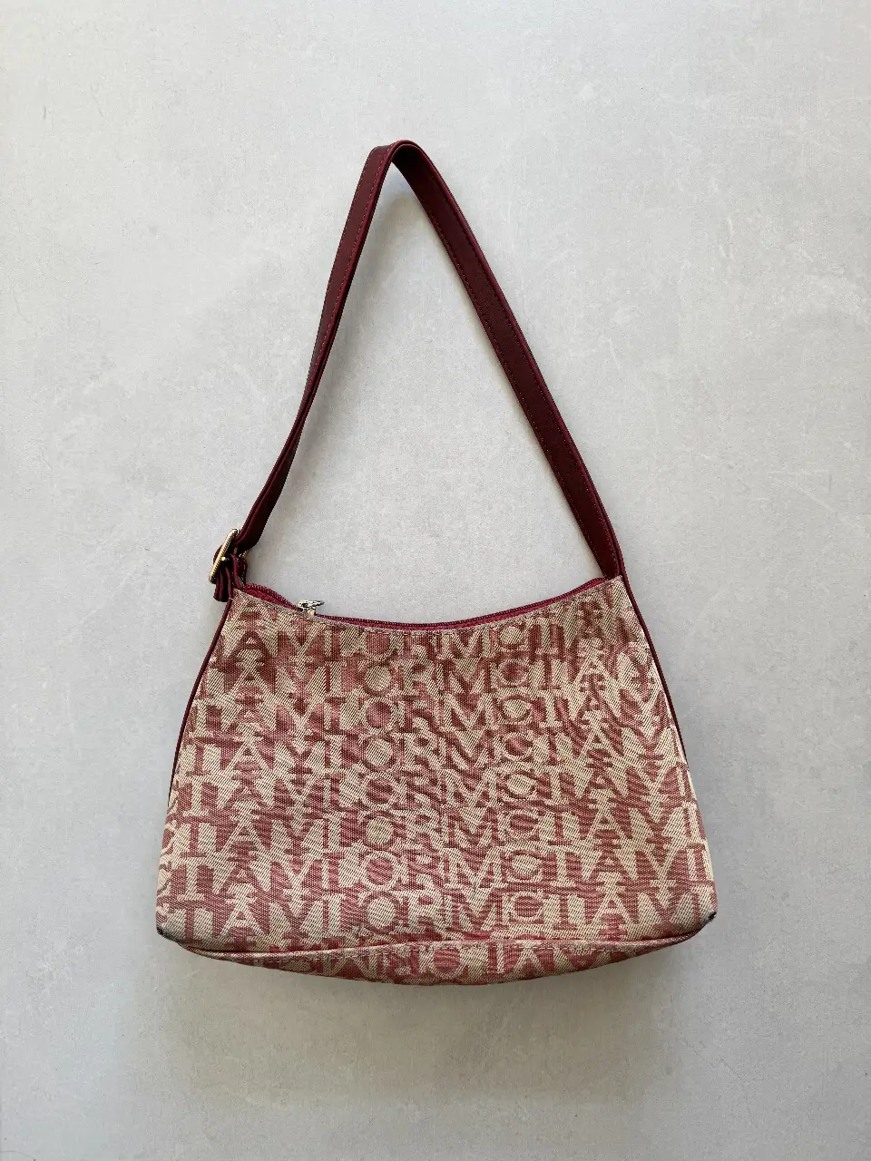 Cartera de hombro Mc Taylor, con estampado del logo de la marca en color rojo y beige y bolsillo interno con cierre. Con correa en color borgoña y detalles dorados. Ideal para un look casual y elegante. Tiene algunos detalles de uso que pueden verse en las últimas fotos. 