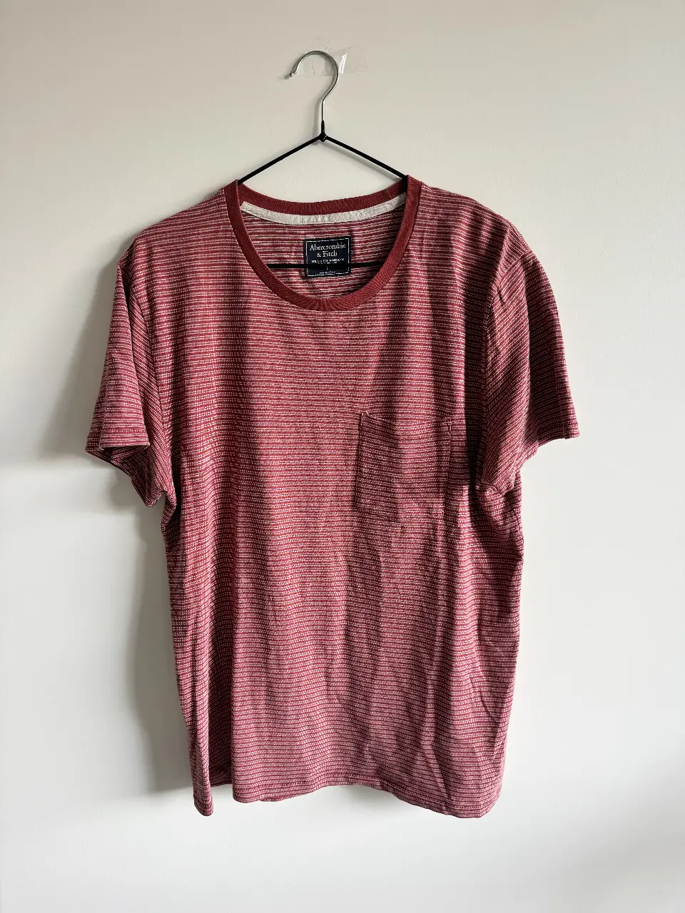 Remera manga corta de hombre, marca Abercrombie & Fitch, con diseño a rayas horizontales en tonos rojos y blancos. Tiene un bolsillo en el pecho y cuello redondo. Ideal para un look casual. Obvio que si sos mujer también podés usarla!🫶🏻Medidas: sisa a sisa 55cm, largo 70cm, hombro a hombro 46cm. 