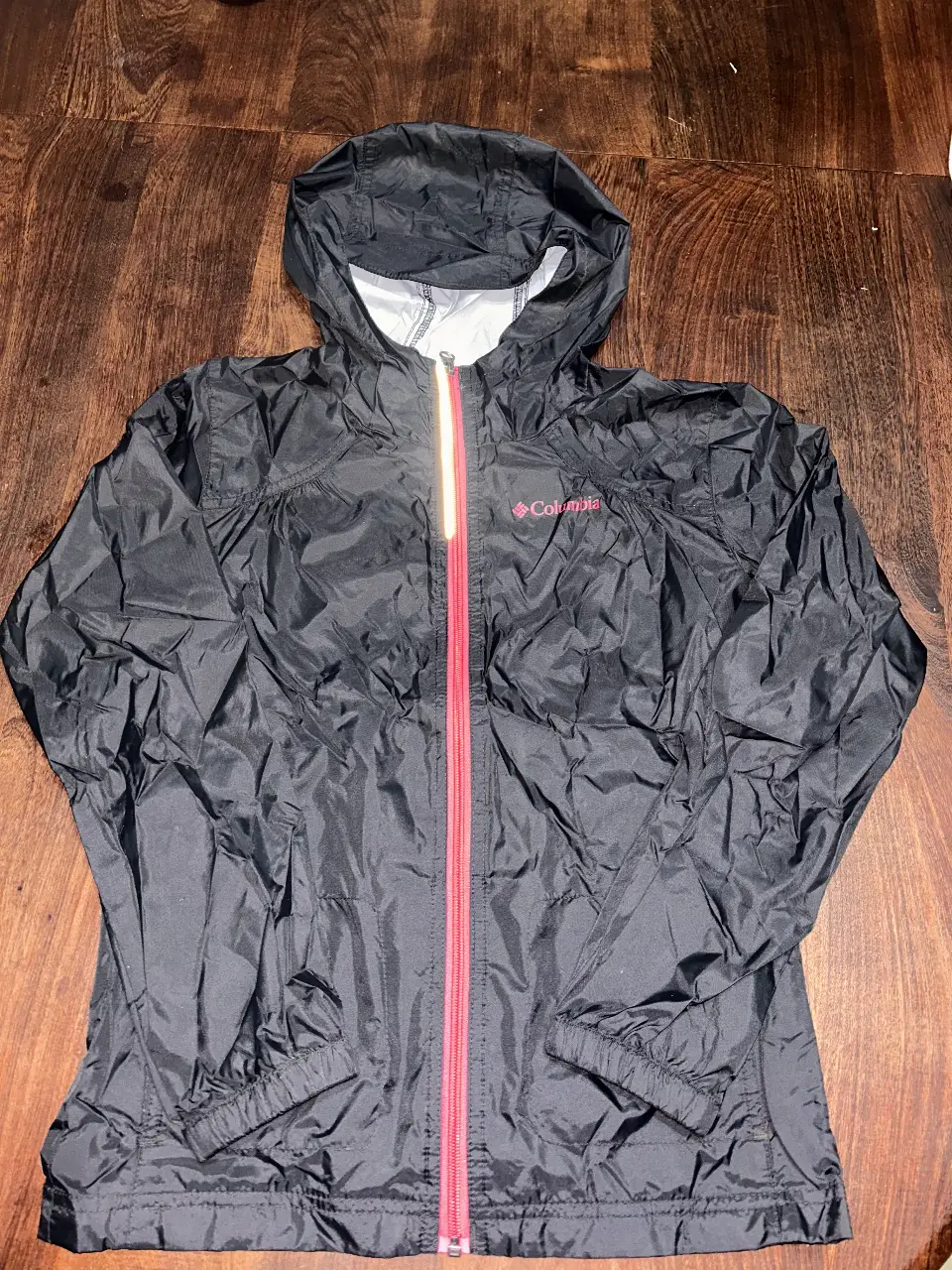 Rompevientos Columbia negro con cierre y detalles en fuccia. Ideal para protegerte de la lluvia y el viento. Cuenta con capucha y un bolsillo interior. Talle M.