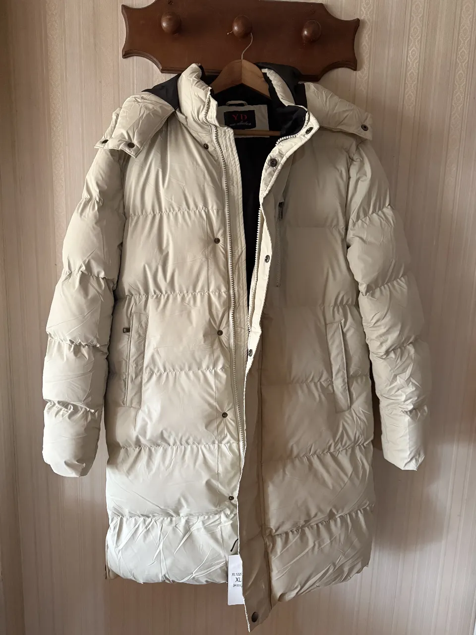 Campera larga de pluma color crudo con capucha. Posee cierre y bolsillos. Ideal para el invierno.