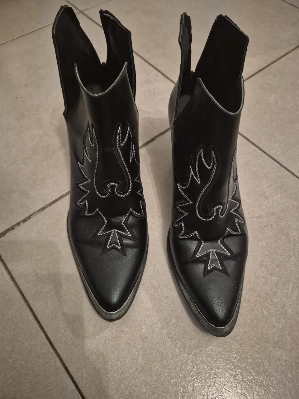 Botines de cuero negro con detalles bordados en blanco. Diseño de punta fina y taco medio. Ideales para un look moderno y audaz.