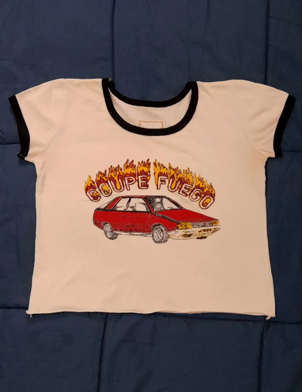 Remera blanca con estampa de auto "Coupe Fuego". Cuello y mangas con borde negro. 

45cm largo
45cm axila a axila
