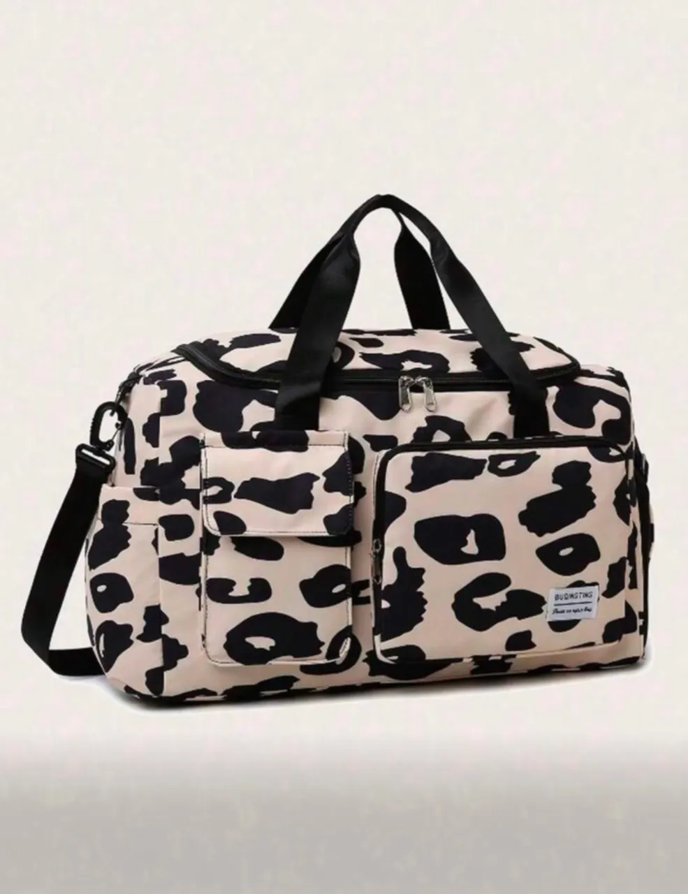 Bolsa de viaje con estampado de leopardo en crudo y negro. Cuenta con dos bolsillos frontales con solapa, asas superiores y una correa desmontable para el hombro. El interior está forrado y tiene un bolsillo con cierre.