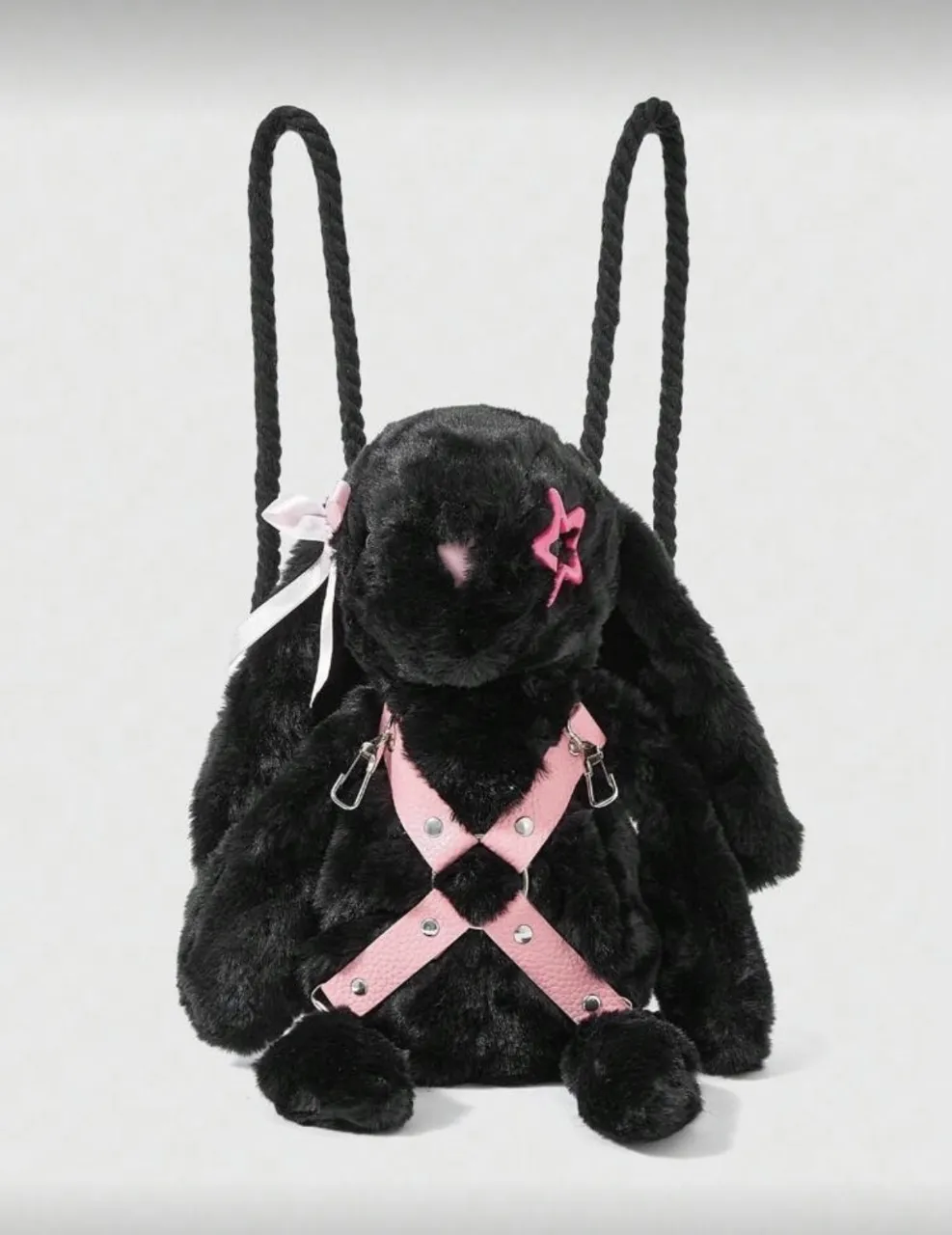 Mochila negra con forma de conejo de peluche. Tiene detalles en rosa como un arnés cruzado en el frente, una estrella en la cabeza y un moño en la oreja. Cierre con detalle de flor.