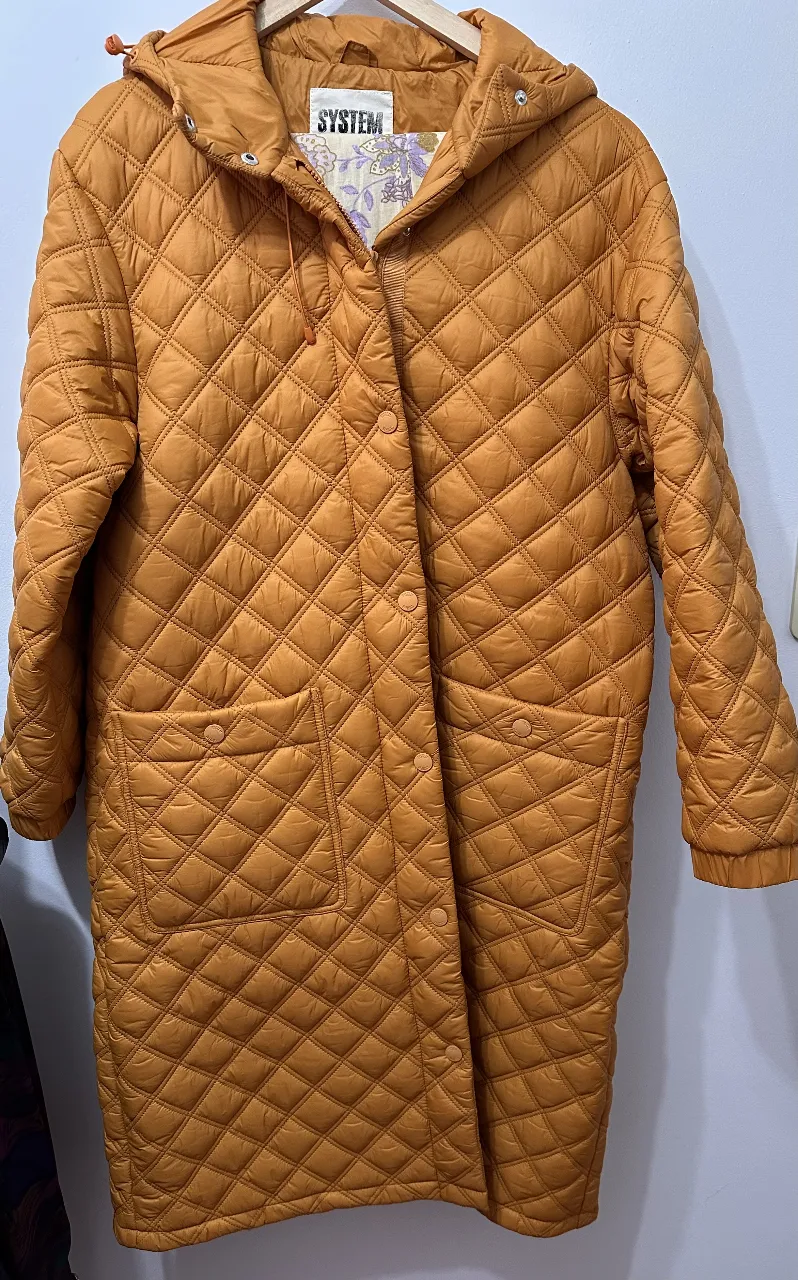 Tapado largo acolchado color naranja con capucha. Posee bolsillos delanteros y cierre con botones. Ideal para el invierno.