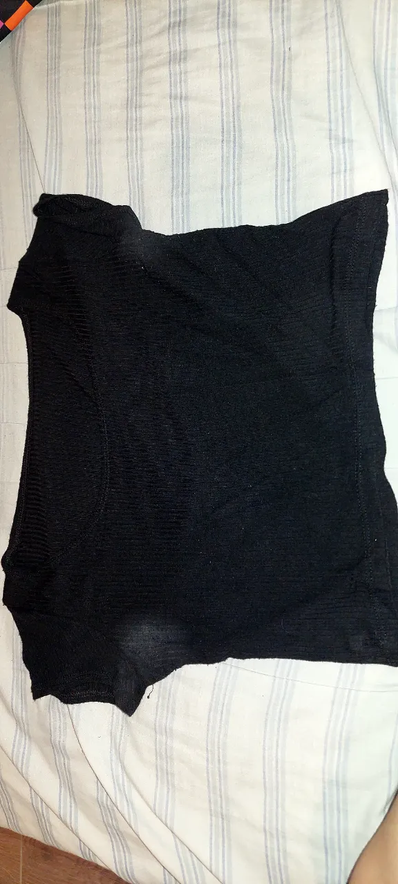 Remera negra de tejido acanalado y detalles deshilachados y manchados en los bordes y axilas.