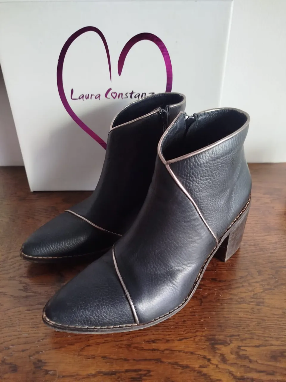 Botitas de cuero negras con detalles de pespunte plateado en el borde superior y en la punta. Taco de madera grueso. Cierre lateral.