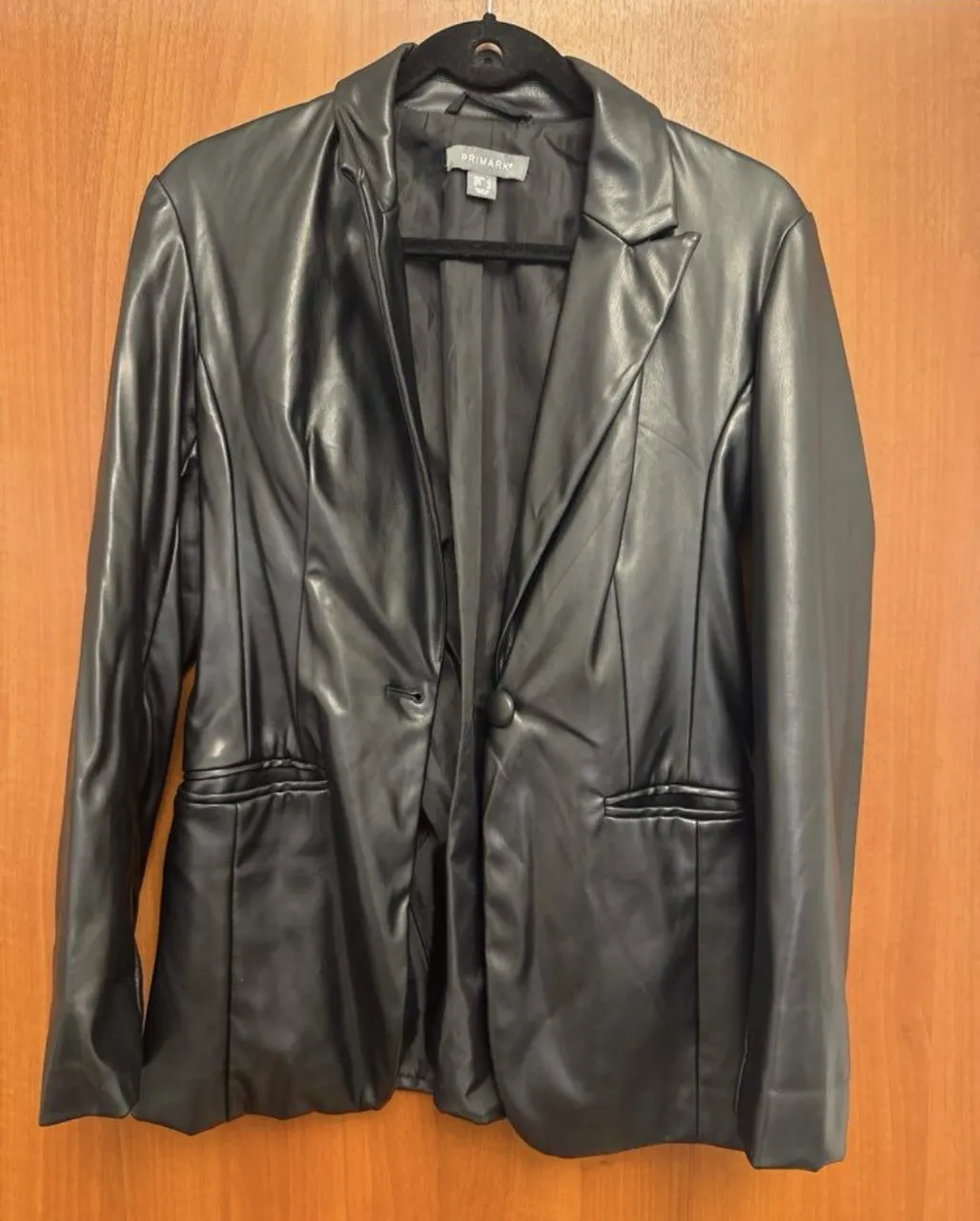 Blazer de cuero sintético negro, con un solo botón y bolsillos delanteros. Ideal para un look elegante y moderno.