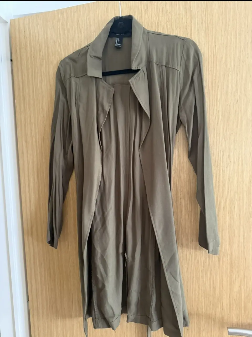 Trench largo de color verde oscuro, ideal para un look casual y elegante. Confeccionado en un tejido ligero y fluido, este trench presenta un diseño abierto con solapas, mangas largas y un cinturón para ajustar la cintura. Perfecto para usar en primavera u otoño.