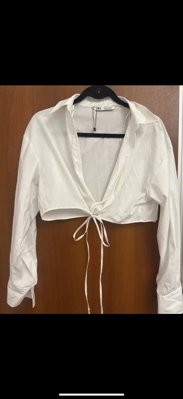 Blusa crop de mujer, blanca, con mangas largas y detalle de lazo en el frente. Marca Zara, ideal para un look casual y moderno.