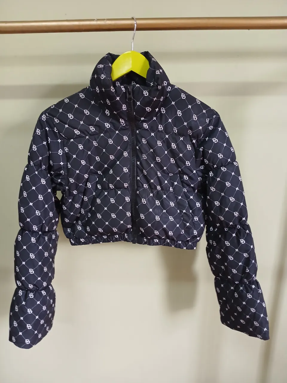 Campera puffer corta negra con estampa de logos blancos repetidos. Posee cuello alto y cierre.